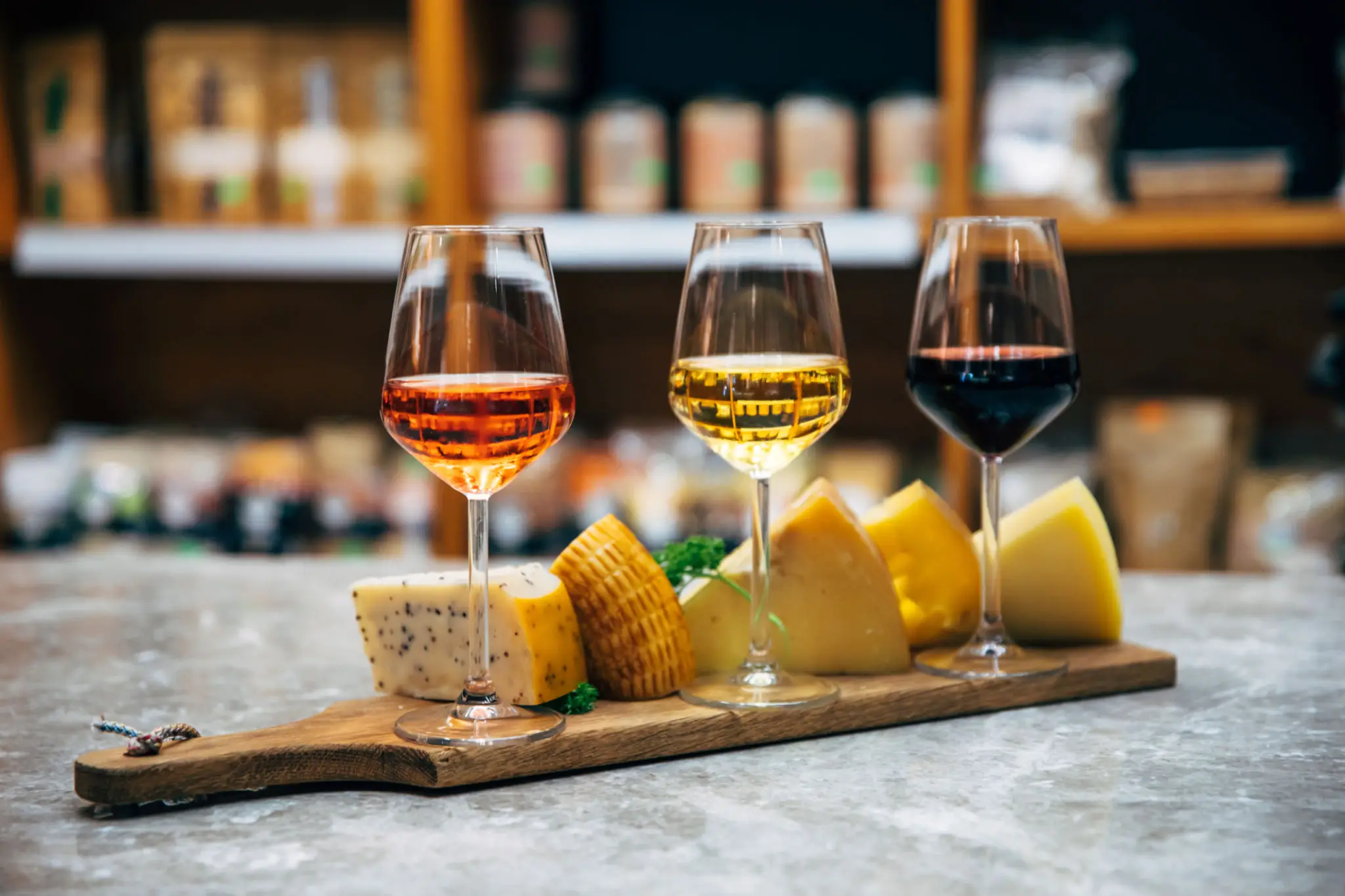 Three glasses of rosé, white, and red wine served with assorted cheese on a wooden board.